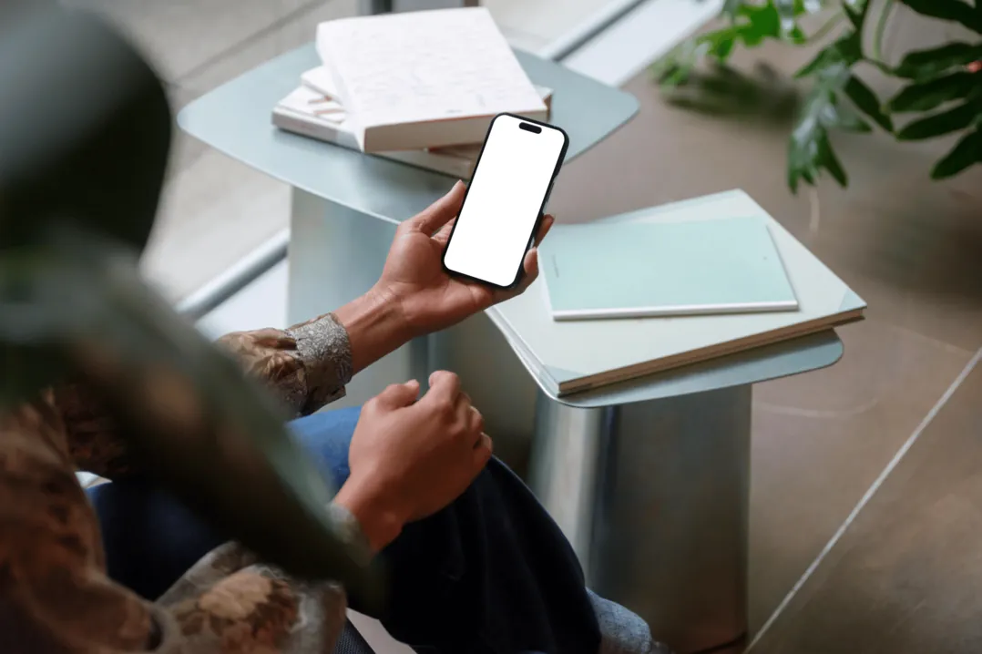 Person am Cafétisch hält ein Smartphone, daneben Notizbücher