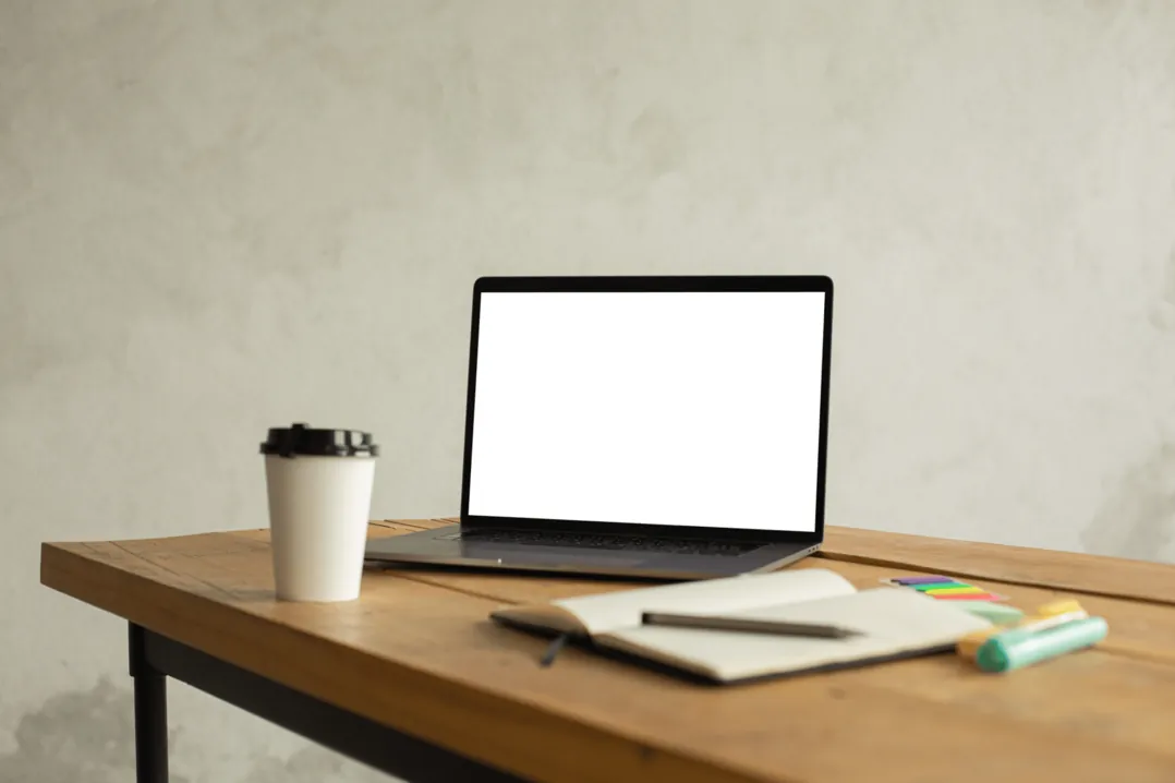 Aufgeklappter Laptop mit Kaffeebecher und Notizblock auf einem Holztisch